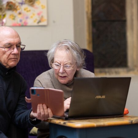 A man and a woman looking at a mobile phone screen and a laptop.