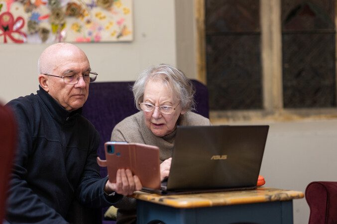 A man and a woman looking at a mobile phone screen and a laptop.