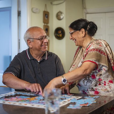 An older couple smiling at each other doing a jigsaw.