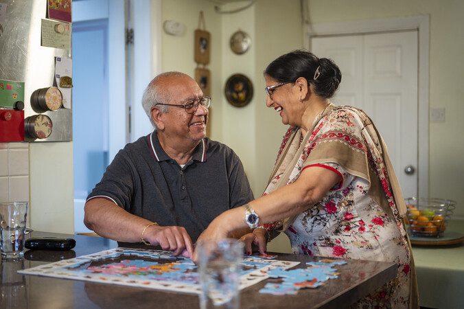 An older couple smiling at each other doing a jigsaw.