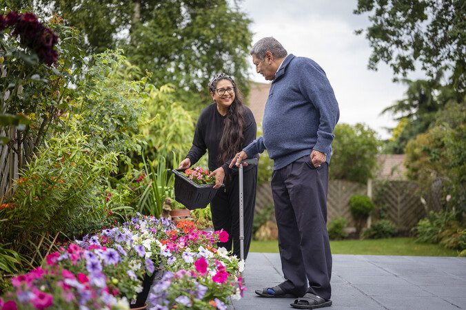 A woman helping a man with a walking stick in the garden.